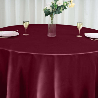 Burgundy round tablecloth on a dining table with wine glasses and a flower vase.