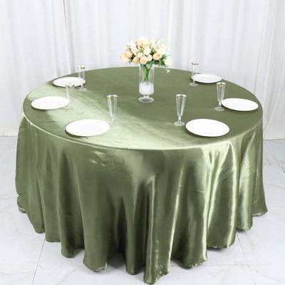 Round olive green tablecloth with plates and glasses on a dining table setting.