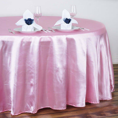Pink satin tablecloth draped over a round table set with elegant napkin displays.