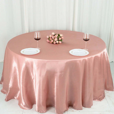 Elegant pink satin tablecloth draped over a round table with wine glasses and roses.