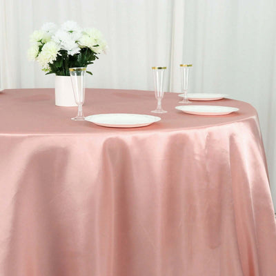 Elegant pink satin tablecloth with white plates and champagne flutes, floral centerpiece.