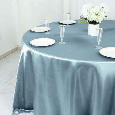 Elegant light blue tablecloth draped over round table with plates and glasses.