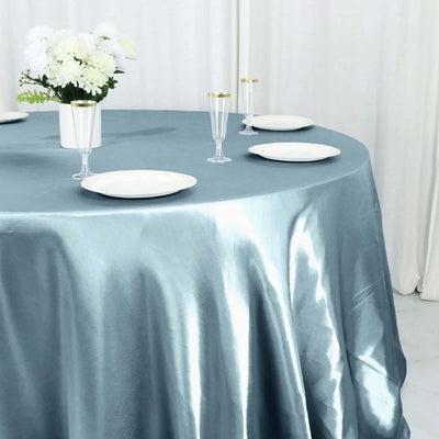 Elegant round table setup with blue satin tablecloth and white dinnerware.