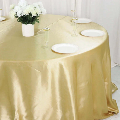 Gold satin tablecloth draping over a round table with plates and a flower centerpiece.