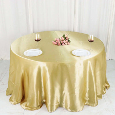 Elegant round gold tablecloth with plates and wine glasses, adorned with pink roses.