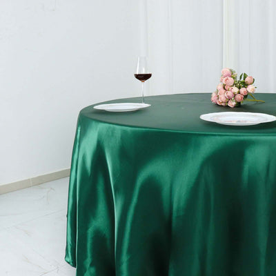 Green satin tablecloth draped over a round table with wine and flowers.
