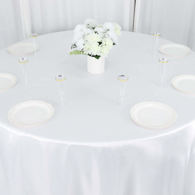 Elegant round table setting with white plates and flowers in a vase.