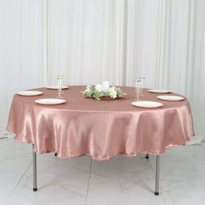 Round table with blush satin tablecloth and white plates set for dining.