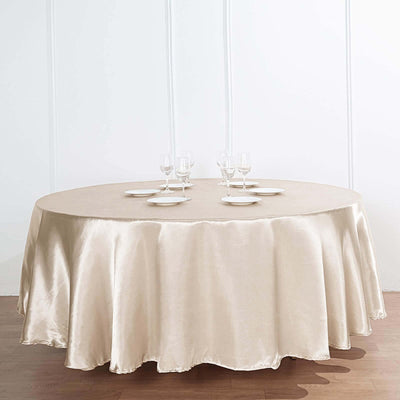 Round beige tablecloth draped elegantly over a table with plates and glasses.