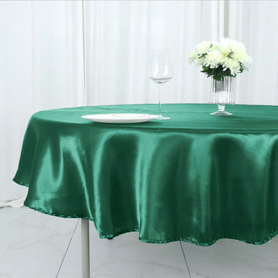 Green satin tablecloth draped over a round table with glassware and flowers.