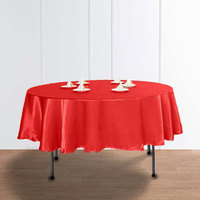 Red round tablecloth with white table decorations on a wooden floor.