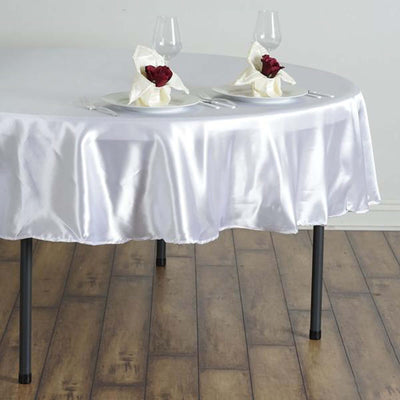 Elegant white satin tablecloth draped on a round table set for a romantic dinner.