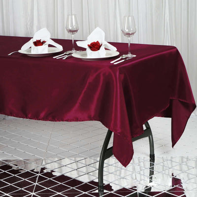 Burgundy satin tablecloth on a dining table set with wine glasses and napkin roses.
