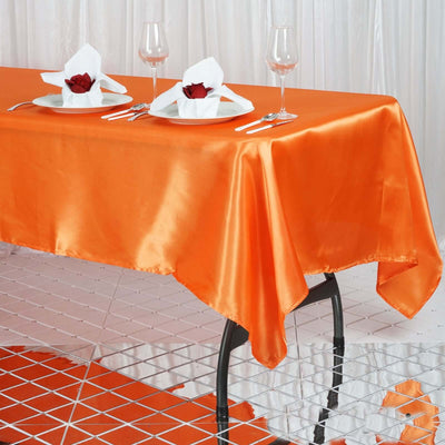 Orange satin tablecloth draped elegantly on a dining table with glasses and plates.