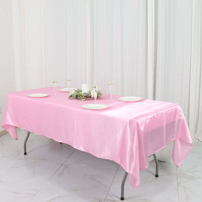 Pink satin tablecloth draped over a table with decorative plates and candles.