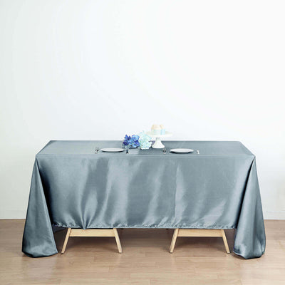 Gray tablecloth draped on a wooden table with plates and decor