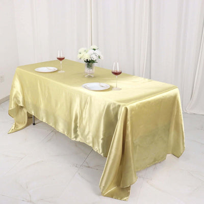 Gold satin tablecloth draped on a dining table with plates and wine glasses.