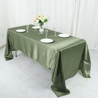Elegant green satin tablecloth draped over a dining table set with plates and glasses.