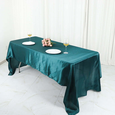 Elegant teal satin tablecloth draped over a dining table with floral centerpiece.