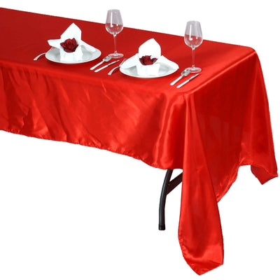 Red satin tablecloth set for elegant dining with plates and glasses.