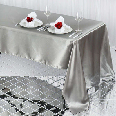 Elegant silver tablecloth set for dining with rose napkins and glassware.