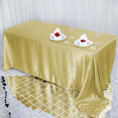 Gold satin tablecloth draped over a table set for dining with plates and glasses.