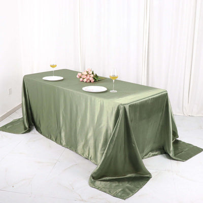 Elegant green satin tablecloth on a dining table with plates and wine glasses.