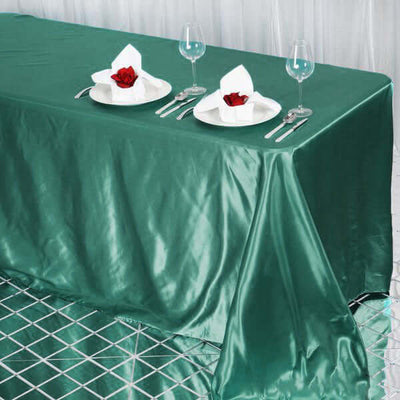 Elegant green tablecloth set for dining with rose-adorned plates and wine glasses.