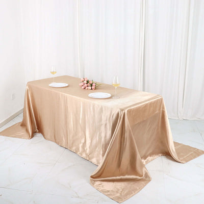 Elegant gold satin tablecloth draped over a table with floral centerpiece and glasses.