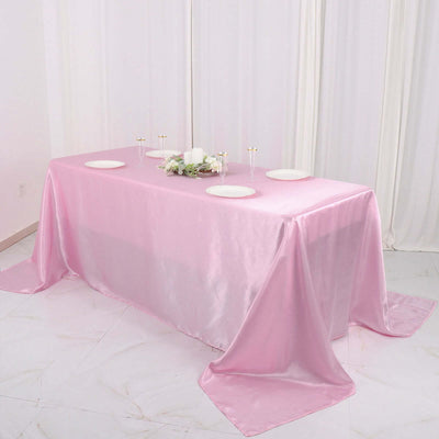 Pink satin tablecloth draped over a table with plates and floral arrangement.