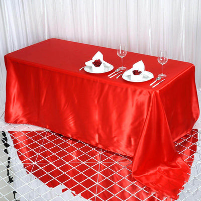 Red satin tablecloth with elegant dining setup featuring plates and wine glasses.