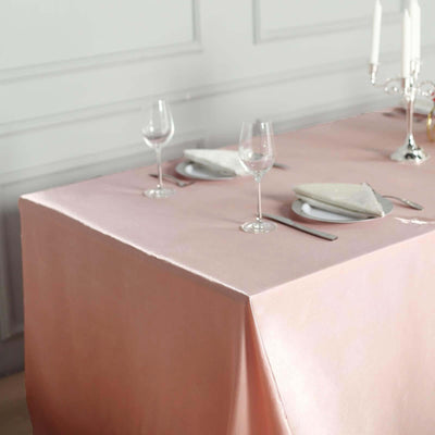 Elegant pink tablecloth set for dining with glassware and plates.