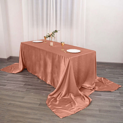 Elegant rose satin tablecloth draped on a dining table with plates and glasses.