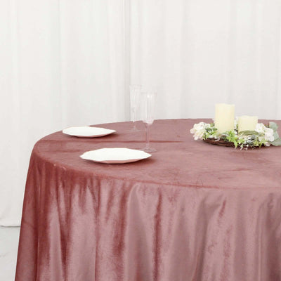 Elegant rose velvet tablecloth on a round table with decorative candles and plates.