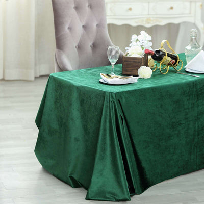 Elegant green tablecloth on a dining table with decor and wine.