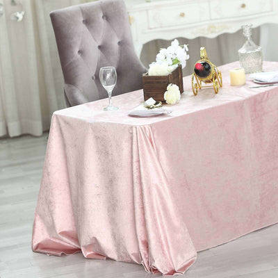 Elegant pink tablecloth draped on a dining table with wine and flowers.