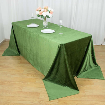 Green velvet tablecloth on a wooden floor with plates and wine glasses.