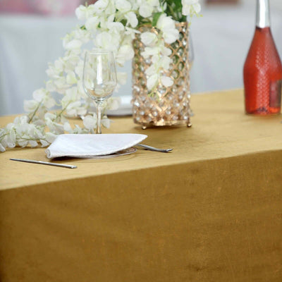 Elegant dining table setup with gold tablecloth, glassware, and floral decor.