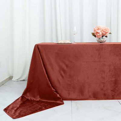 Elegant rust tablecloth draped on a table with floral centerpiece and wine glass.