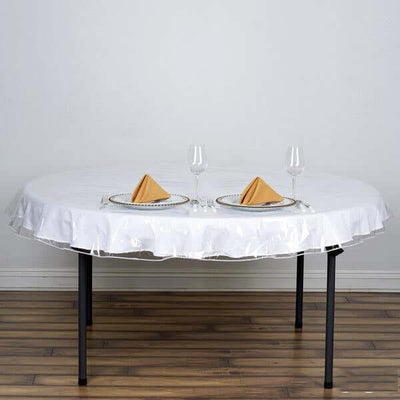 Round white tablecloth on a dining table with glasses and napkins.