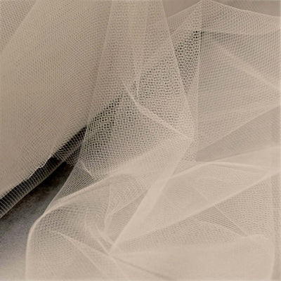 Sheer beige tulle fabric draped elegantly, showcasing its delicate texture.