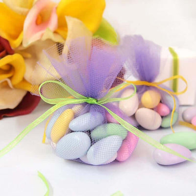 Pastel candy-filled mesh bags with decorative ribbons on a plain backdrop.