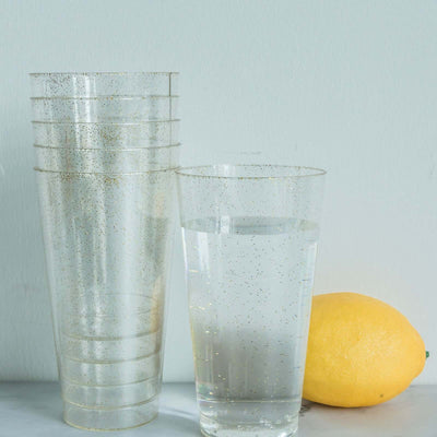 Clear plastic cups with glitter, stacked with a glass of water and a lemon.