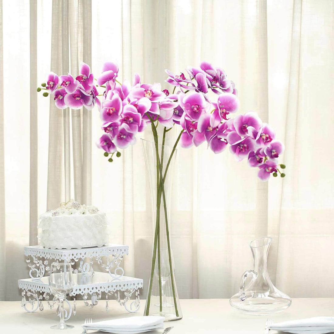 Purple orchids in a glass vase on a table with a cake and glassware.