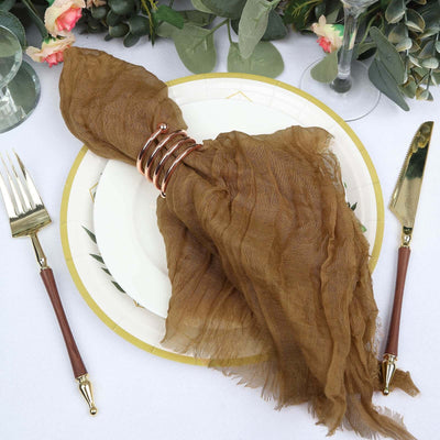 Brown sheer napkin with a gold napkin ring on a decorative plate.