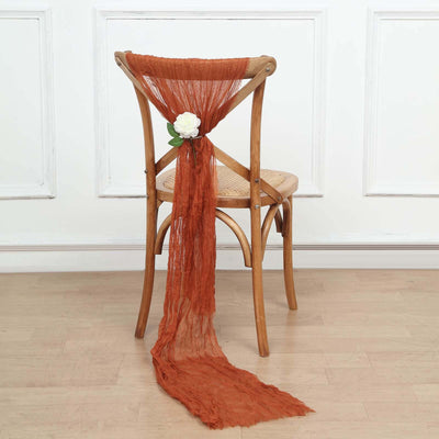 Rust-colored sheer fabric draped on a wooden chair with a flower accent.
