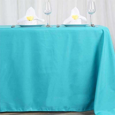 Turquoise tablecloth draping over a table set with glasses and folded napkins.