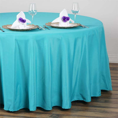 Turquoise tablecloth draping over a round table set with plates and glasses.