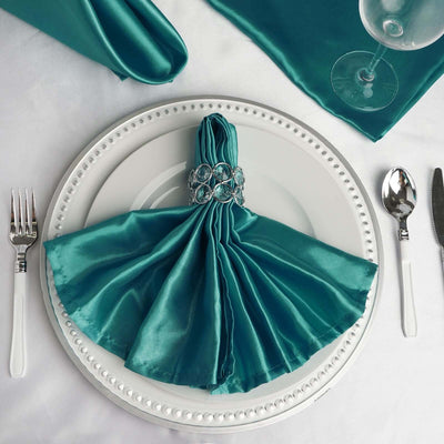 Elegant teal napkin folded in a fan shape on a white plate with decorative ring.