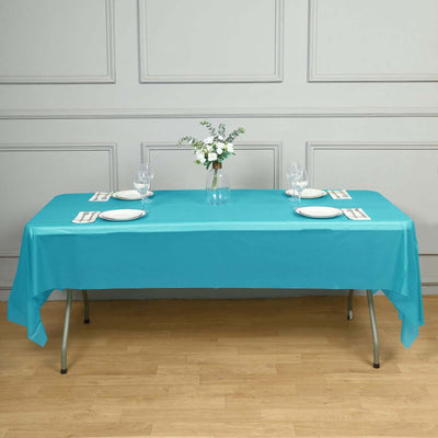Turquoise tablecloth set on a dining table with plates and glasses.